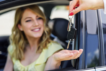 An attractive woman in a car gets the car keys. Rent or purchase of auto.