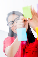 Portrait of young Asian employee looking at multiple reminders while planning her work in the office