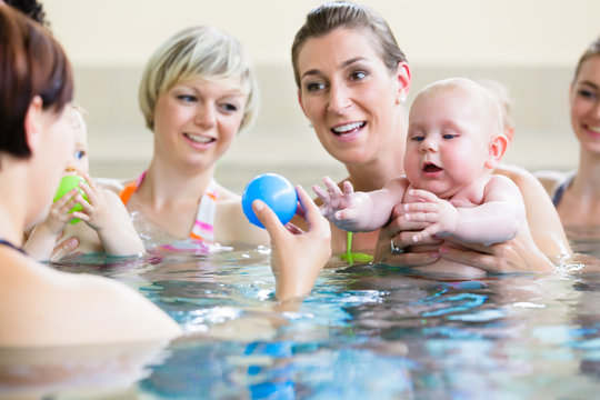 Small kids and their mothers playing with balls at baby swimming course