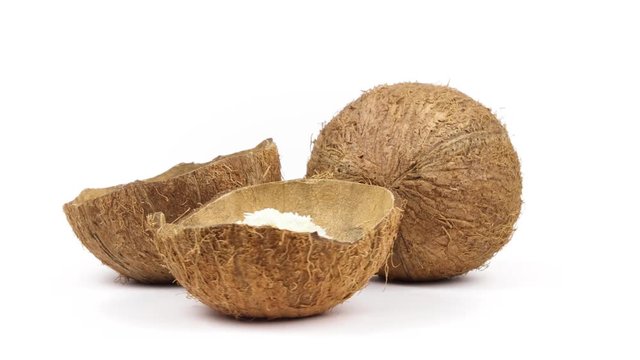 One whole and two shells halves of tropical coconut with dried white coconut flakes rotating on white isolated background. Healthy tropical fruits. Loopable seamless cocos rotating