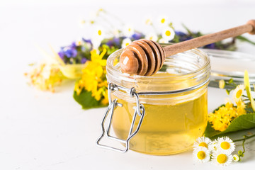 Honey  in a jar with wild herbs on white