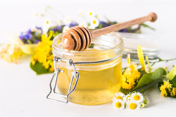 Honey  in a jar with wild herbs on white