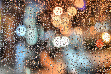 Drops of rain against the blue glass. Blurred street of the night city. Autumnal abstract background