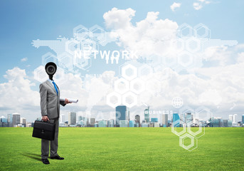 Camera headed man standing on green grass against modern cityscape