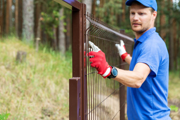 worker installing welded metal mesh fence