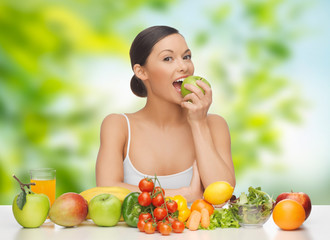 diet, healthy food and people concept - woman eating green apple with vegetables and fruits on table over green natural background