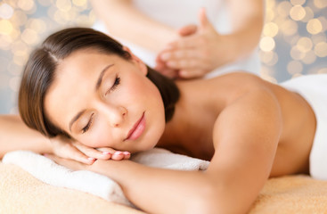 Fototapeta na wymiar wellness, spa and beauty concept - close up of beautiful woman having massage over holidays lights background