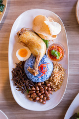 Nasi Lemak is a Malay fragrant rice dish cooked in coconut milk and butterfly pea served with fried chicken, fried small fish, roasted peanut, boiled egg and krupuk.