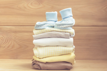 blue baby shoes on clothes stack. Pastel clothes for baby infant on wooden background. Newborn.