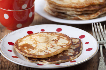 Pancakes in white plate in red peas and red coffee cups