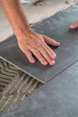 Worker placing ceramic floor tiles on adhesive surface