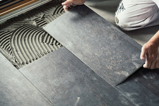 Worker placing dark grey ceramic floor tiles on adhesive surface