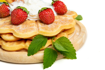 Close-up of a waffle pile on a wooden board decorated with cream, strawberries and mint leaves.