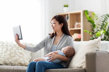 family, technology and motherhood concept - happy smiling young asian mother with sleeping baby and tablet pc computer at home