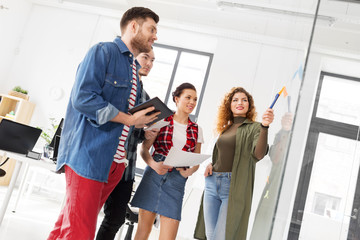 business, startup, planning and people concept - happy creative team discussing something on glass board at office