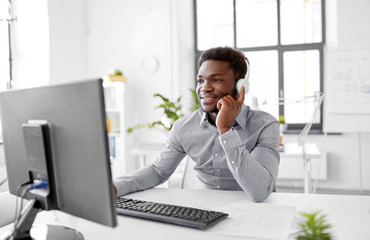 business, technology and people concept - happy african american businessman with headphones and computer listening to music at office