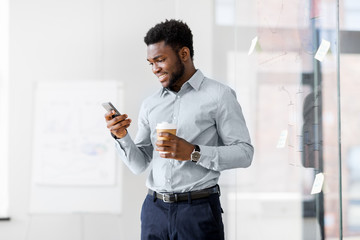 business, people and technology concept - african american businessman with smartphone having break and drinking coffee at office