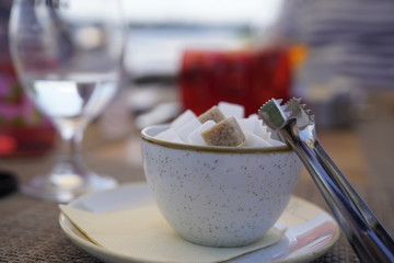 Close up white and brown sugar cubes in a bowl with a metallic pincers at the restaurant