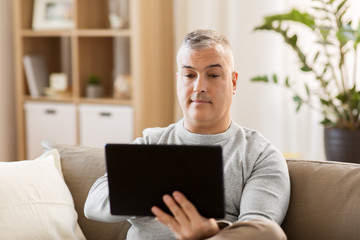 technology, people and lifestyle concept - man with tablet pc computer sitting on sofa at home