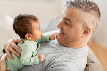 family, fatherhood and people concept - happy father with little baby boy sitting on sofa at home
