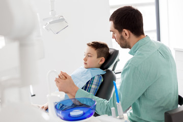 medicine, dentistry and healthcare concept - father supporting son at dental clinic