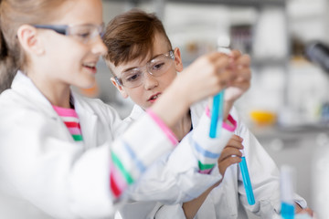 education, science and children concept - kids with test tubes studying chemistry at school laboratory
