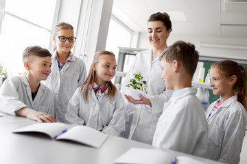 Fototapeta na wymiar education, science and school concept - kids or students and teacher with plant at biology class