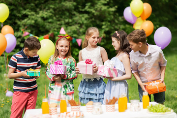 holidays, childhood and celebration concept - happy kids with gifts on birthday party at summer garden