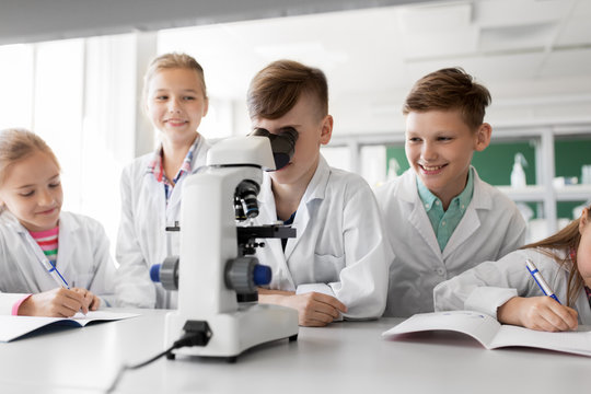 education, science and children concept - kids or students with microscope studying biology at school laboratory