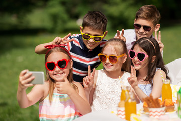 holidays, childhood and technology concept - happy kids in sunglasses taking selfie on birthday party at summer garden