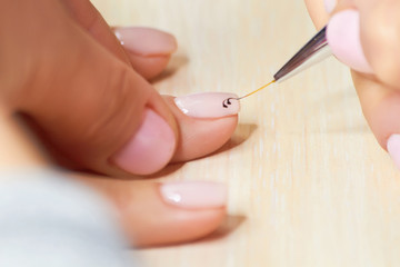 Manicurist drawing pattern on nails. Beautician drawing lace pattern on clients nails. The process of receiving manicure in beauty salon.