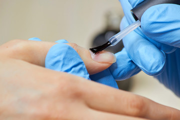 Procedure of applying colorless varnish. Manicurist hands applying transparent nail polish on healthy female nails.