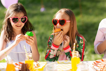 holidays, childhood and celebration concept - happy kids in sunglasses sitting at table on birthday...