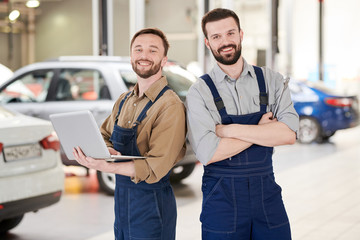 Waist up portrait of two handsome bearded workers smiling at camera while posing in production workshop of modern car factory, copy space