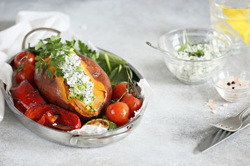 Oven baked sweet potato served with herbs cream cheese filling and roasted vegetables. Super food, clean eating, plant based concept.