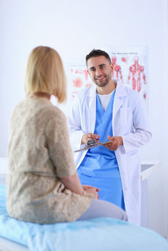 Handsome doctor is talking with young female patient and making notes while sitting in his office
