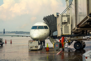 Small jet airplane with attached jetway at airport gate terminal during storm delay