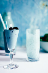 Blue Majik smooothie on tall glass with colored straw, over a blue colored wooden board against a clear background