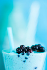 Blue Majik smooothie on tall glass with colored straw, over a blue colored wooden board against a clear background