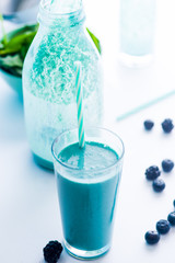 Blue Majik smooothie on tall glass with colored straw, over a blue colored wooden board against a clear background