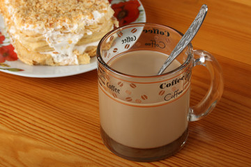 Plate with puff cake and transparent glass cup with coffee and milk