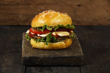 Hamburger on a wooden board against a dark background with copy space. Hamburger with sauce and fresh vegetables on a wooden table. Burger.