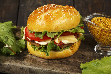 Hamburger on a wooden board against a dark background with copy space. Hamburger with sauce and fresh vegetables on a wooden table. Burger.