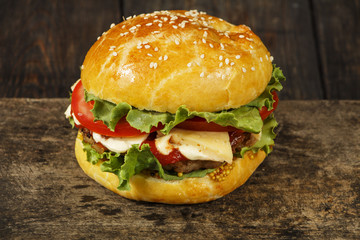Hamburger on a wooden board against a dark background with copy space. Hamburger with sauce and fresh vegetables on a wooden table. Burger.