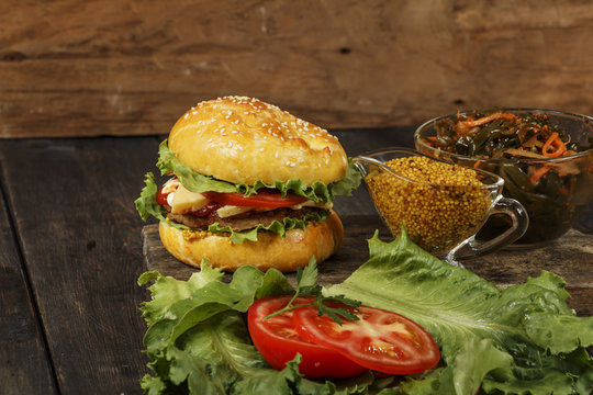 Hamburger on a wooden board against a dark background with copy space. Hamburger with sauce and fresh vegetables on a wooden table. Burger.