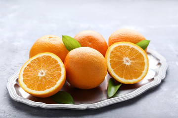 Orange fruit with green leafs in tray on grey wooden table