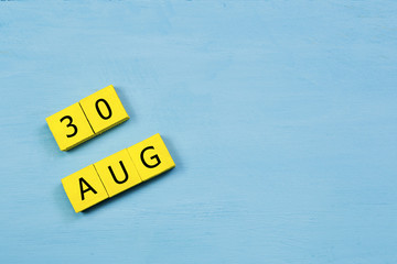 AUG 30, yellow cube calendar on blue wooden surface with copy space