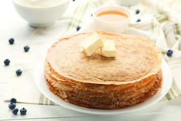 Heap of pancakes in plate with butter on white wooden table