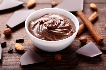 Melted chocolate in bowl with nuts and cinnamon on wooden table