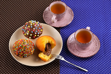 Baking with tea and chocolate on the table.  Two cups of tea with cupcakes and chocolate with a multicolored powder on the table.
